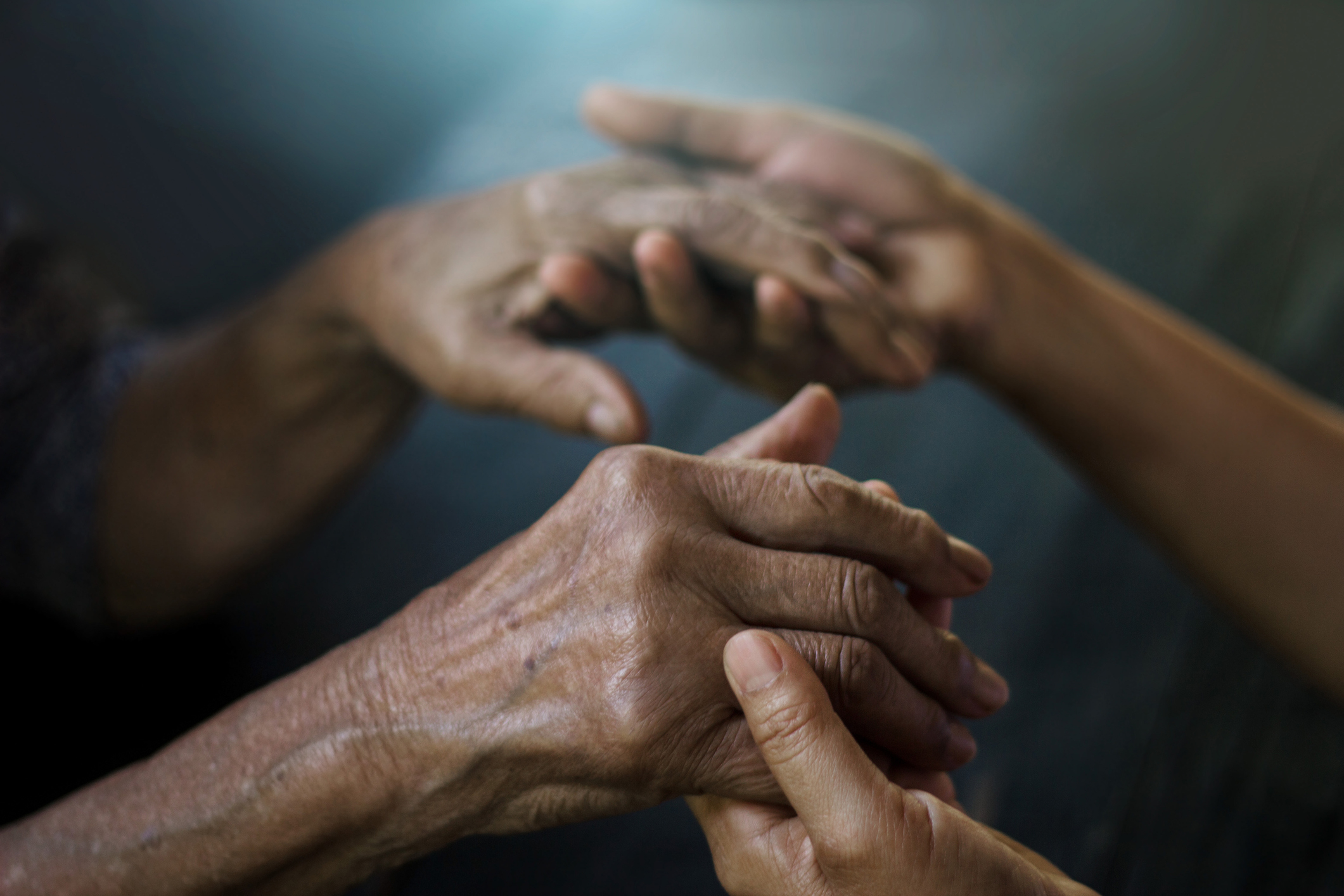 Two pairs of hands, one older and one younger, gently holding each other symbolizing care and support