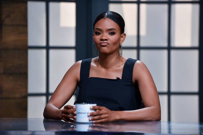 Candace Owens sitting at a desk in a sleeveless black top, holding a coffee cup, with a contemplative expression