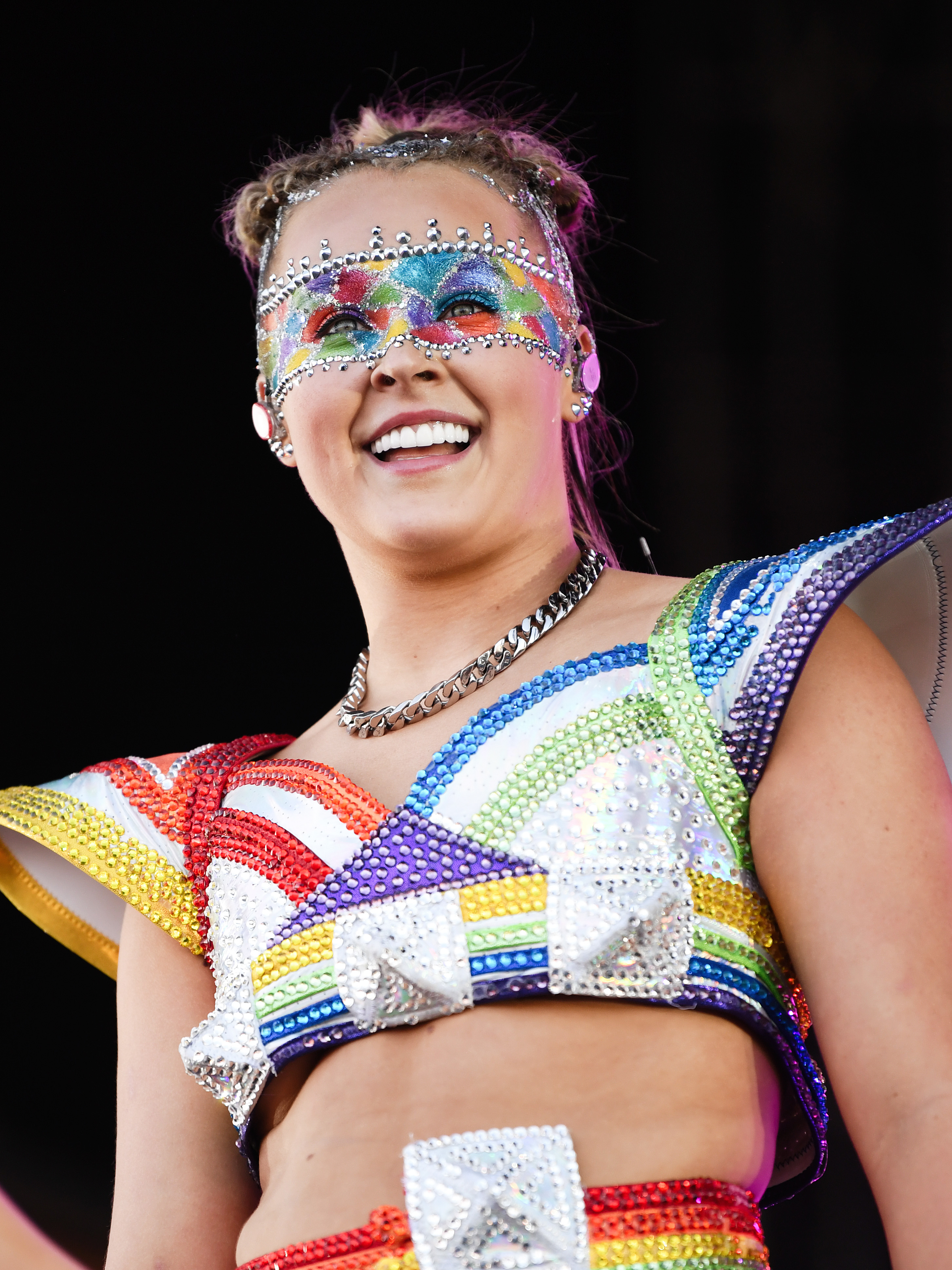 JoJo Siwa wearing a vibrant, gem-studded outfit with bold geometric patterns and a matching mask at an event