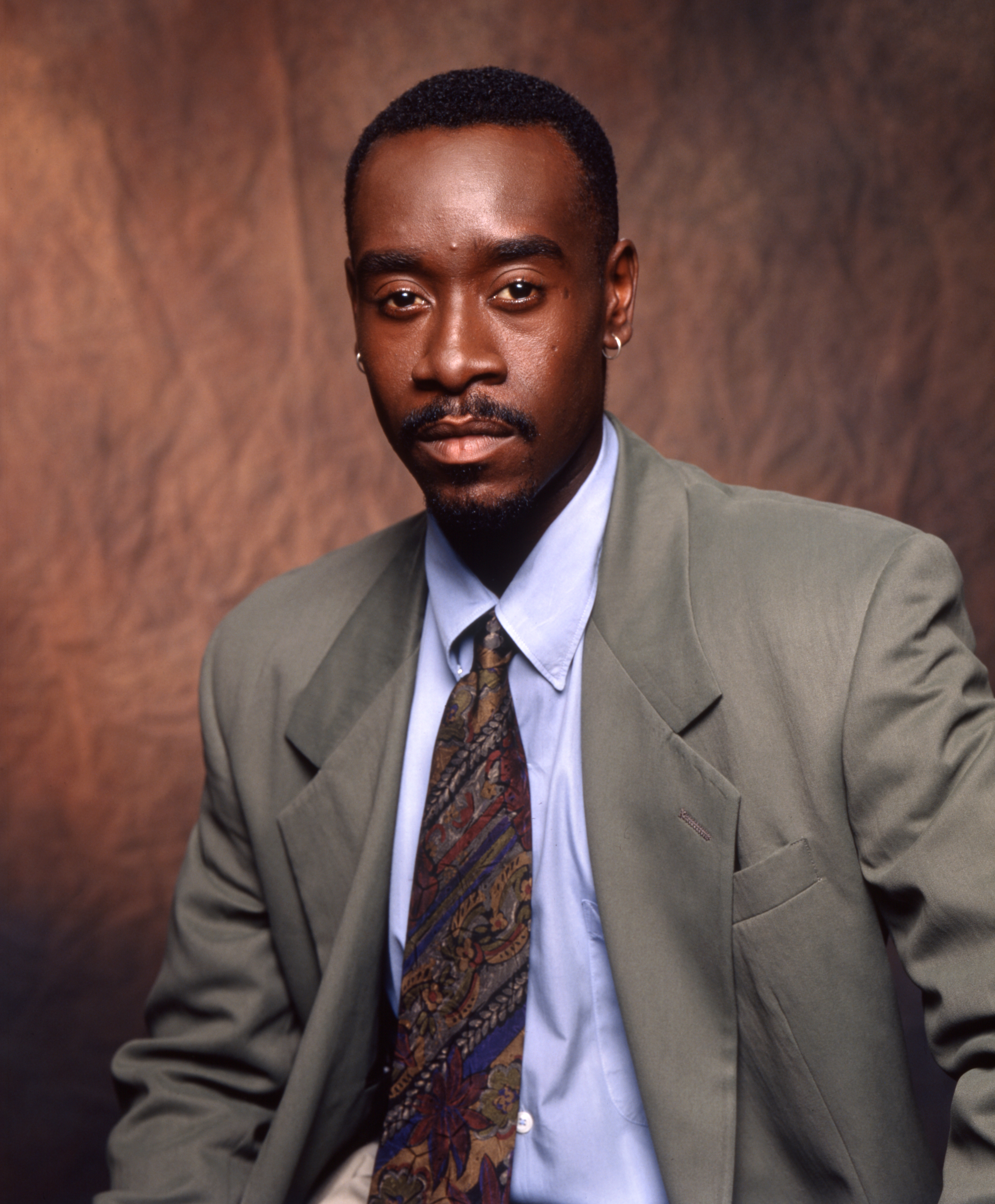 Don Cheadle in a suit with a paisley tie, posing against a textured studio background