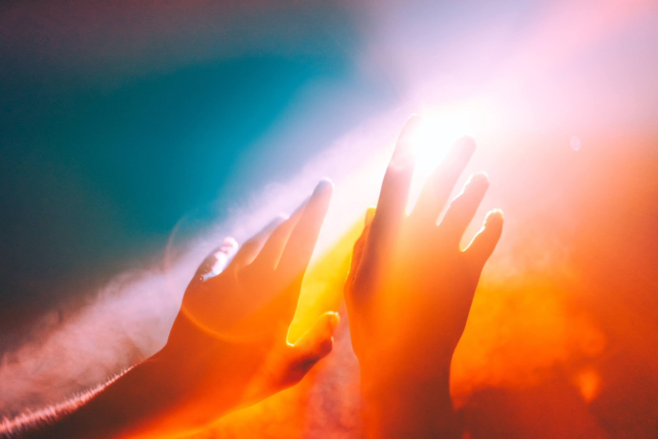 Two hands reaching towards a bright light with a foggy, abstract background