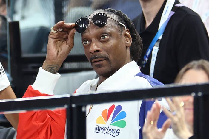 Snoop Dogg adjusts his sunglasses while seated at an Olympic event