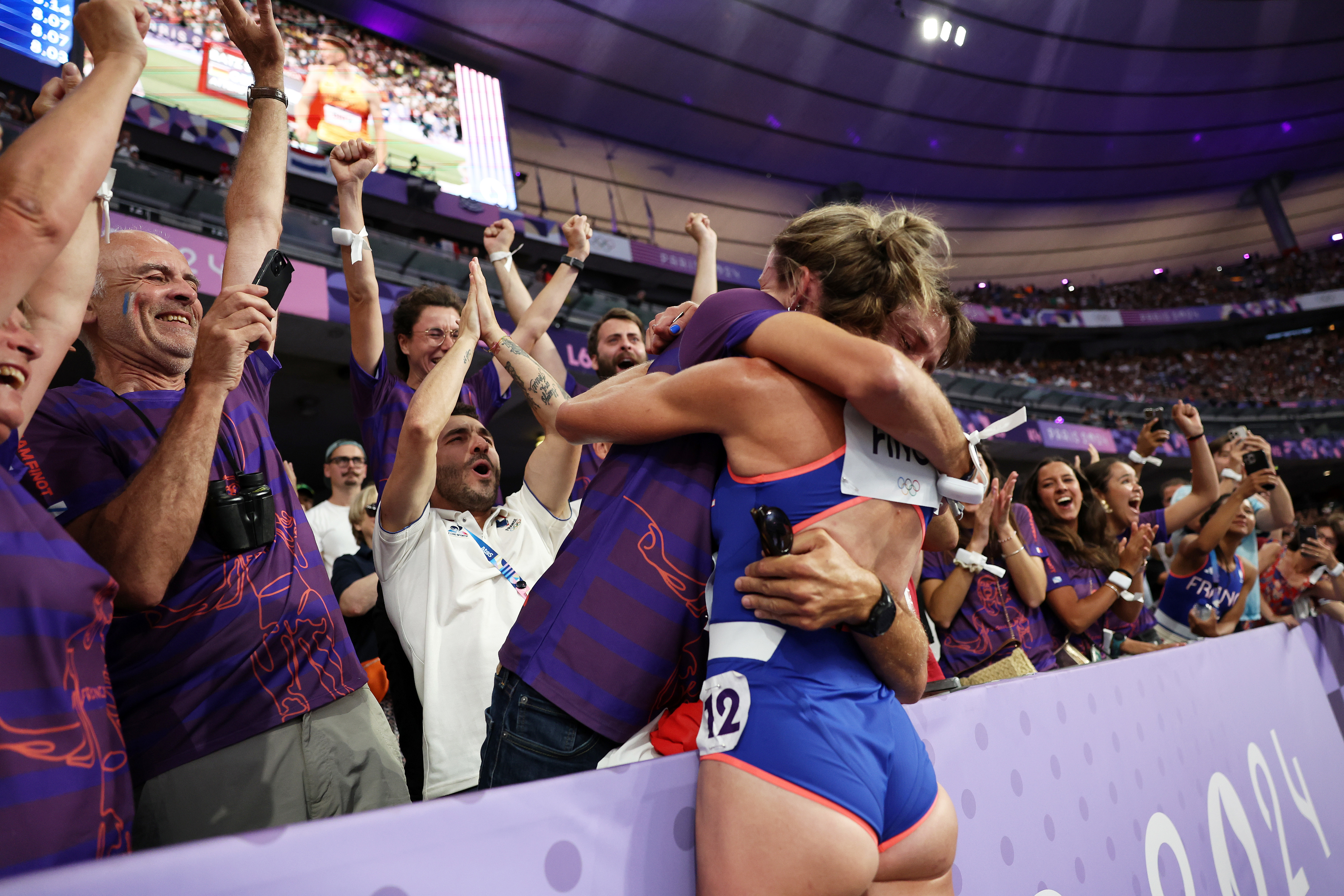 Track athlete celebrating with two fans after a competition inside a stadium, surrounded by a cheering crowd