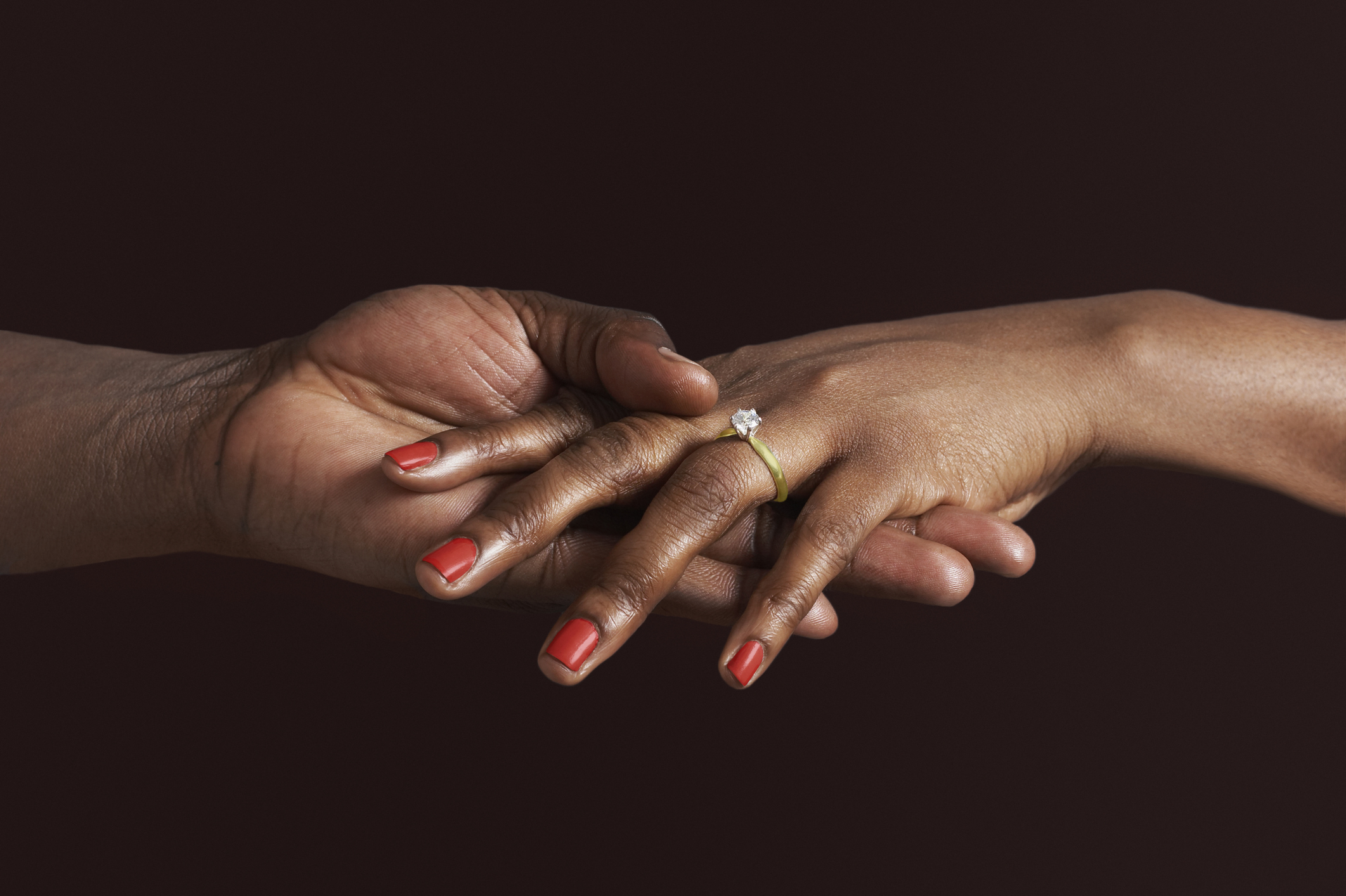Two hands touching, one with a diamond engagement ring and painted nails