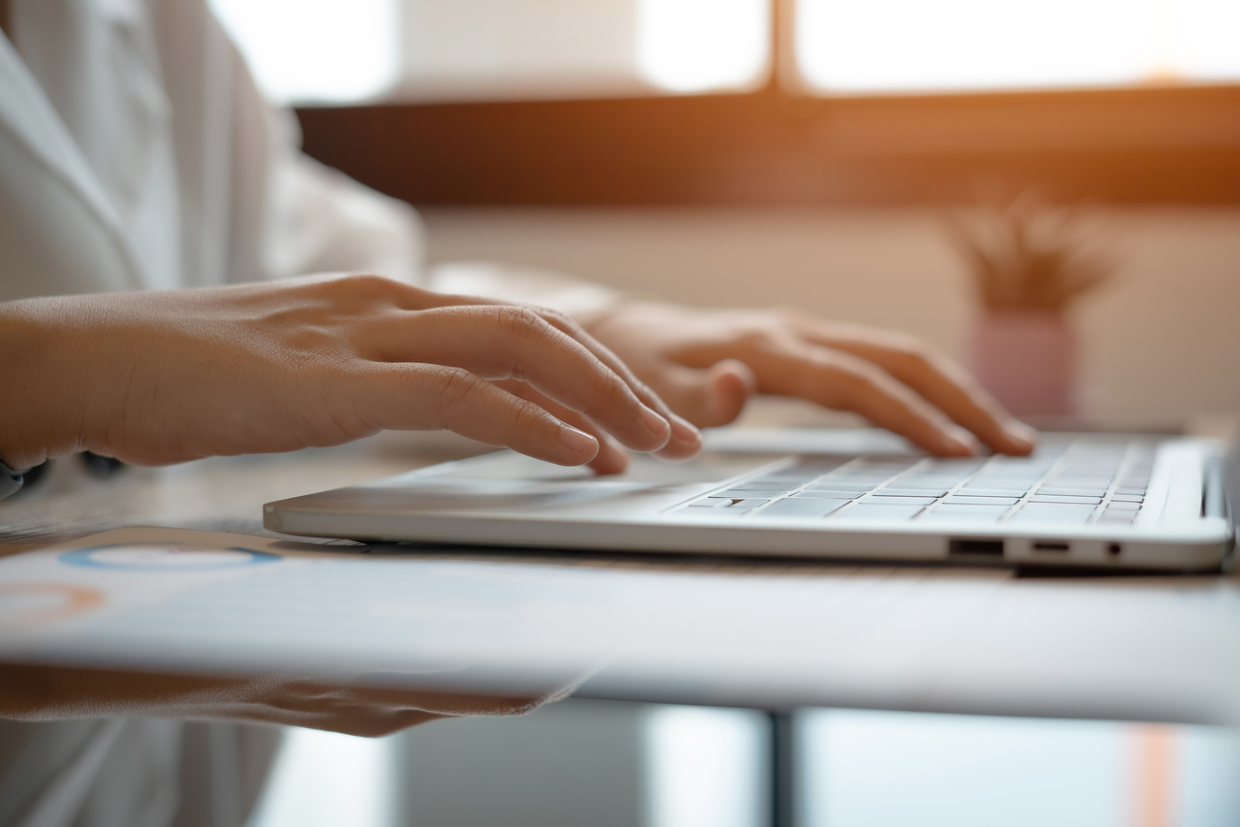 Person typing on a laptop keyboard at a desk with documents nearby