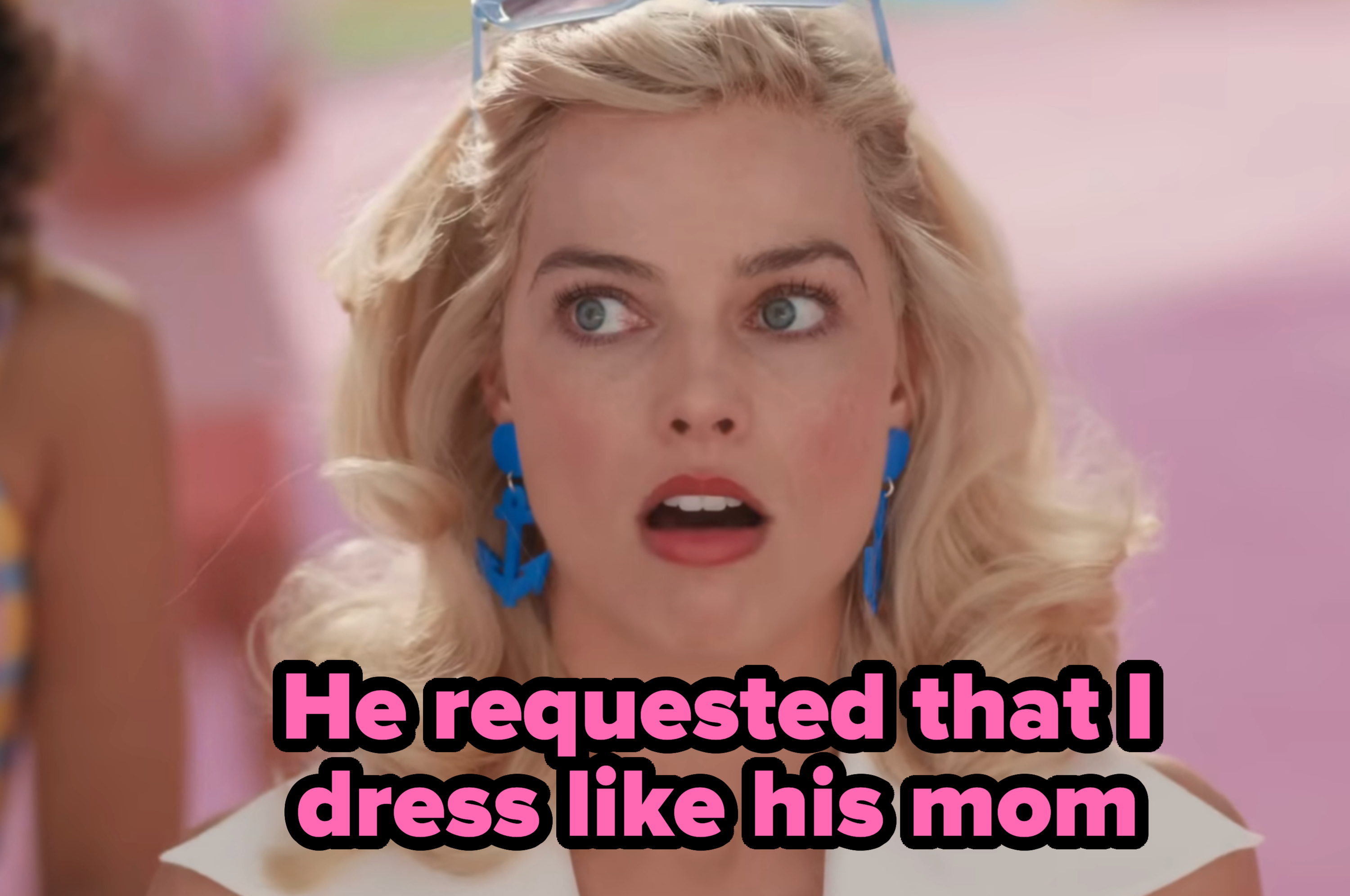 Margot Robbie, wearing blue anchor-shaped earrings and white sleeveless top, looks surprised in a close-up shot