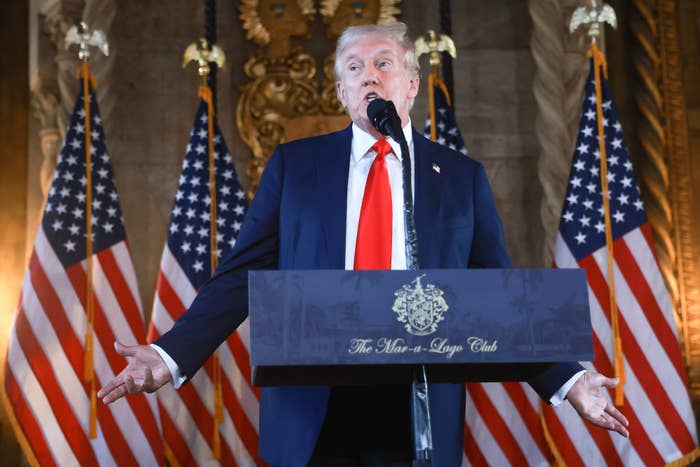 Donald Trump speaks at a podium with &quot;The Mar-a-Lago Club&quot; inscription, flanked by American flags and a gold emblem in the background