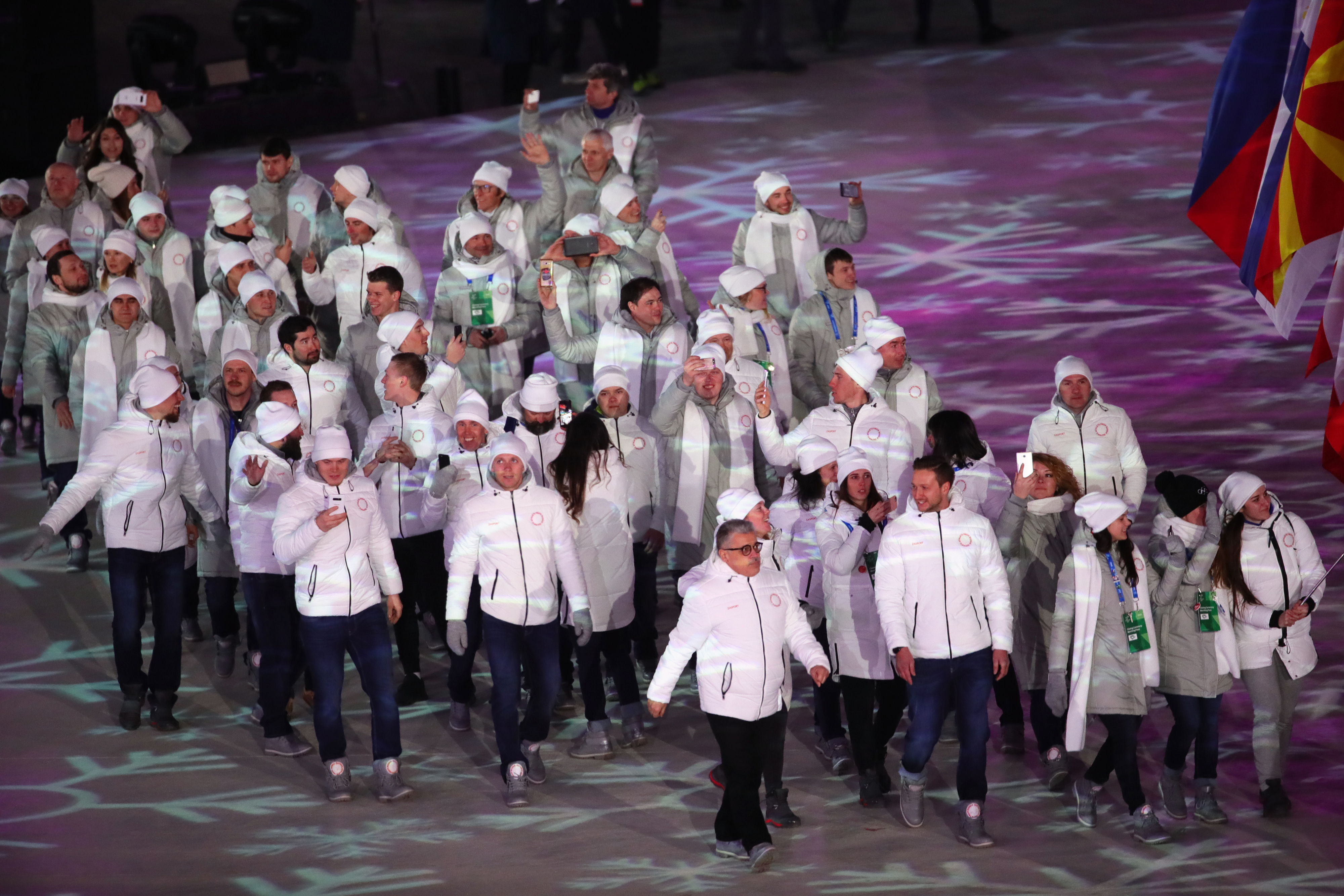 Athletes of the team Olympic Athletes from Russia (OAR) in winter gear march together. Large flags are visible in the background
