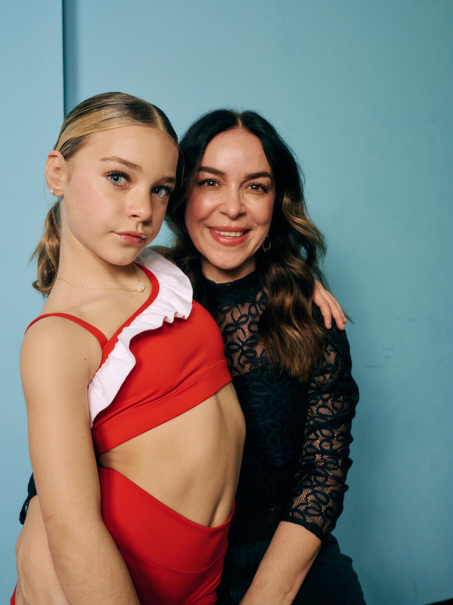 Young girl in a stylish dance outfit poses with an adult woman in a lace top, both smiling warmly for the camera