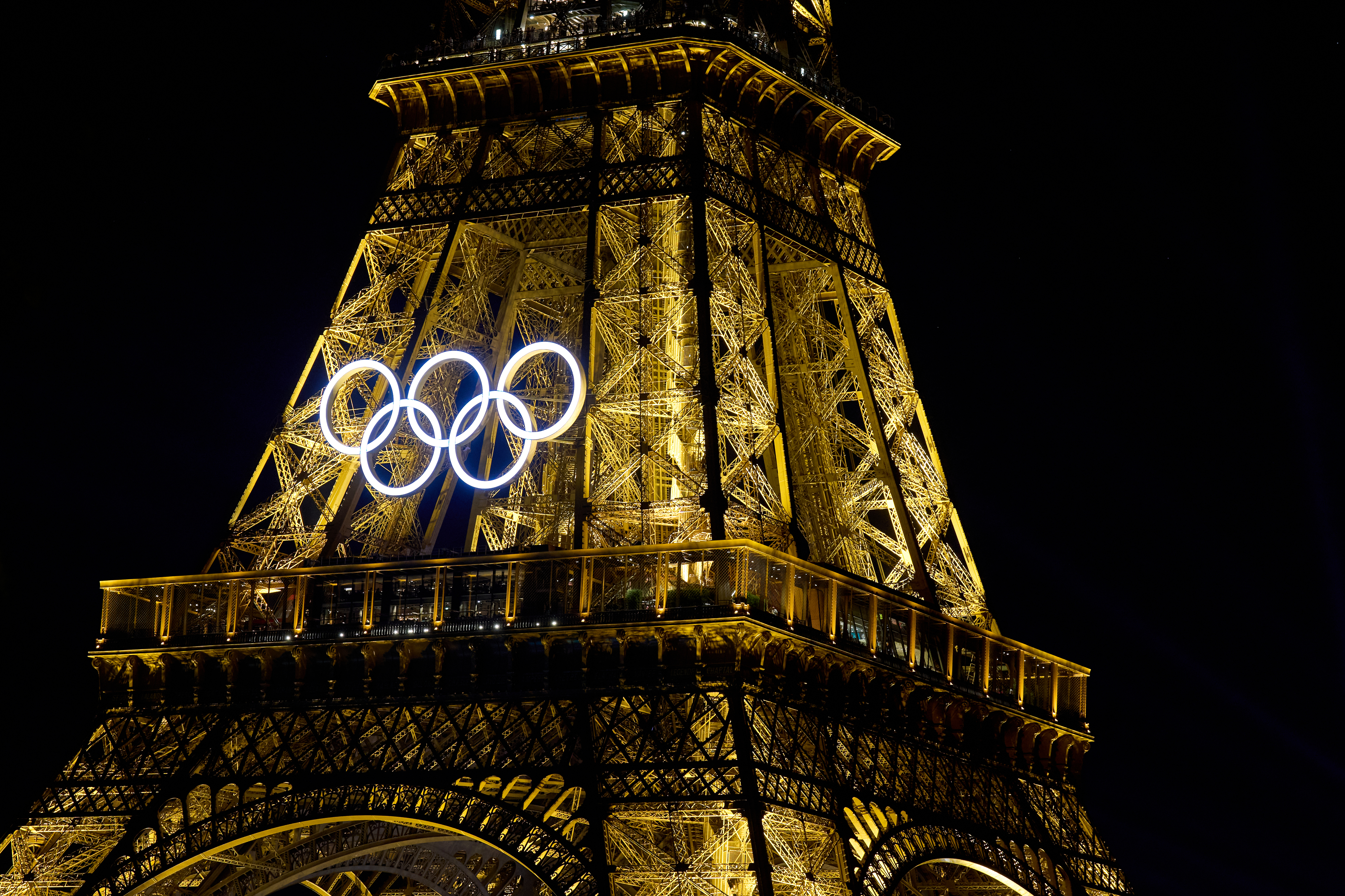 The Eiffel Tower lit up at night with the Olympic rings suspended in the middle, symbolizing the hosting of the upcoming Olympic Games