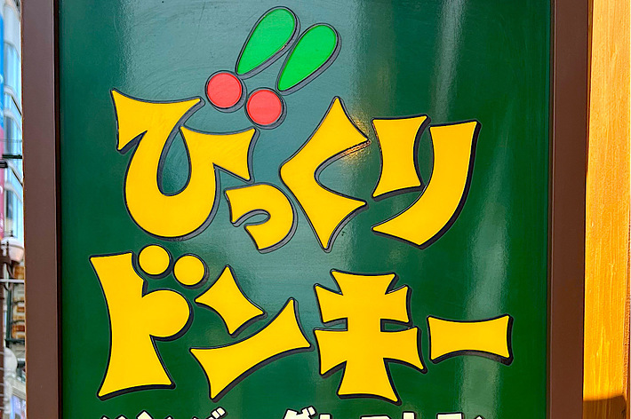 A sign for Bikkuri Donkey, a hamburger restaurant, with the restaurant name in yellow text and a small orange sign at the bottom with a power outlet symbol