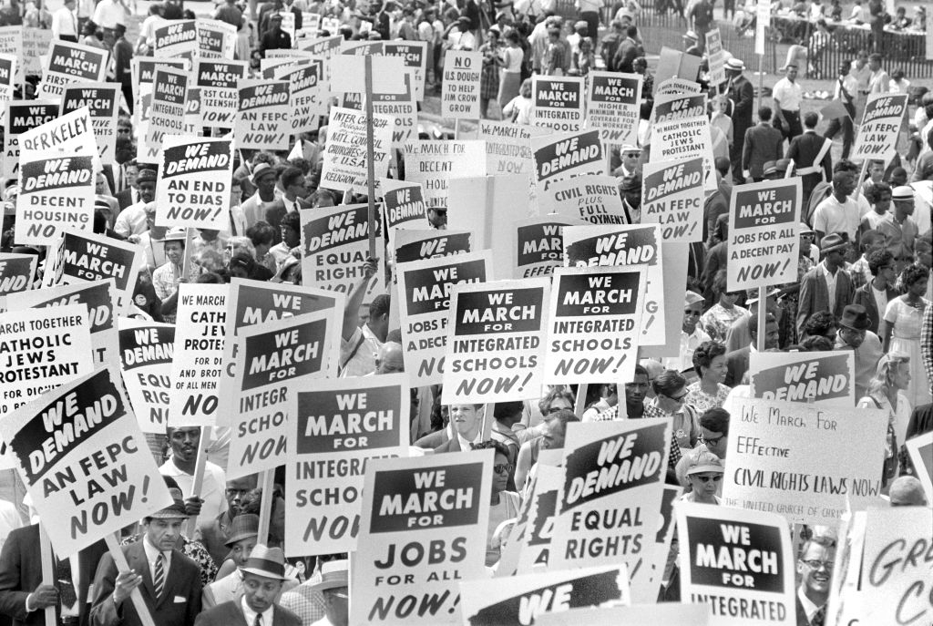 Crowd at the 1963 March on Washington holding signs with messages like "We March for Jobs and Freedom" and "We Demand Equal Rights Now!"