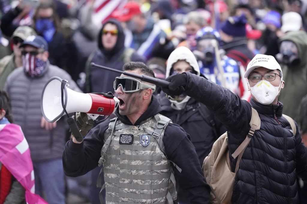 A man with a megaphone and another holding a microphone stand in a crowd of protestors wearing masks and goggles
