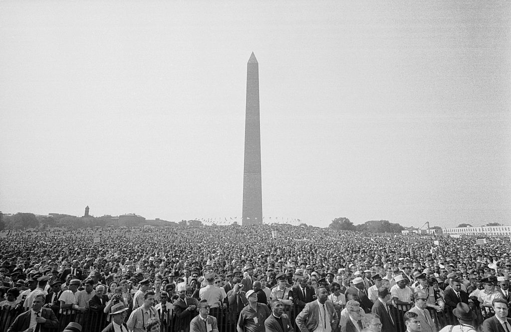 A large crowd gathers in front of the Washington Monument in Washington, D.C., likely during a historic event or protest. No identifiable individuals