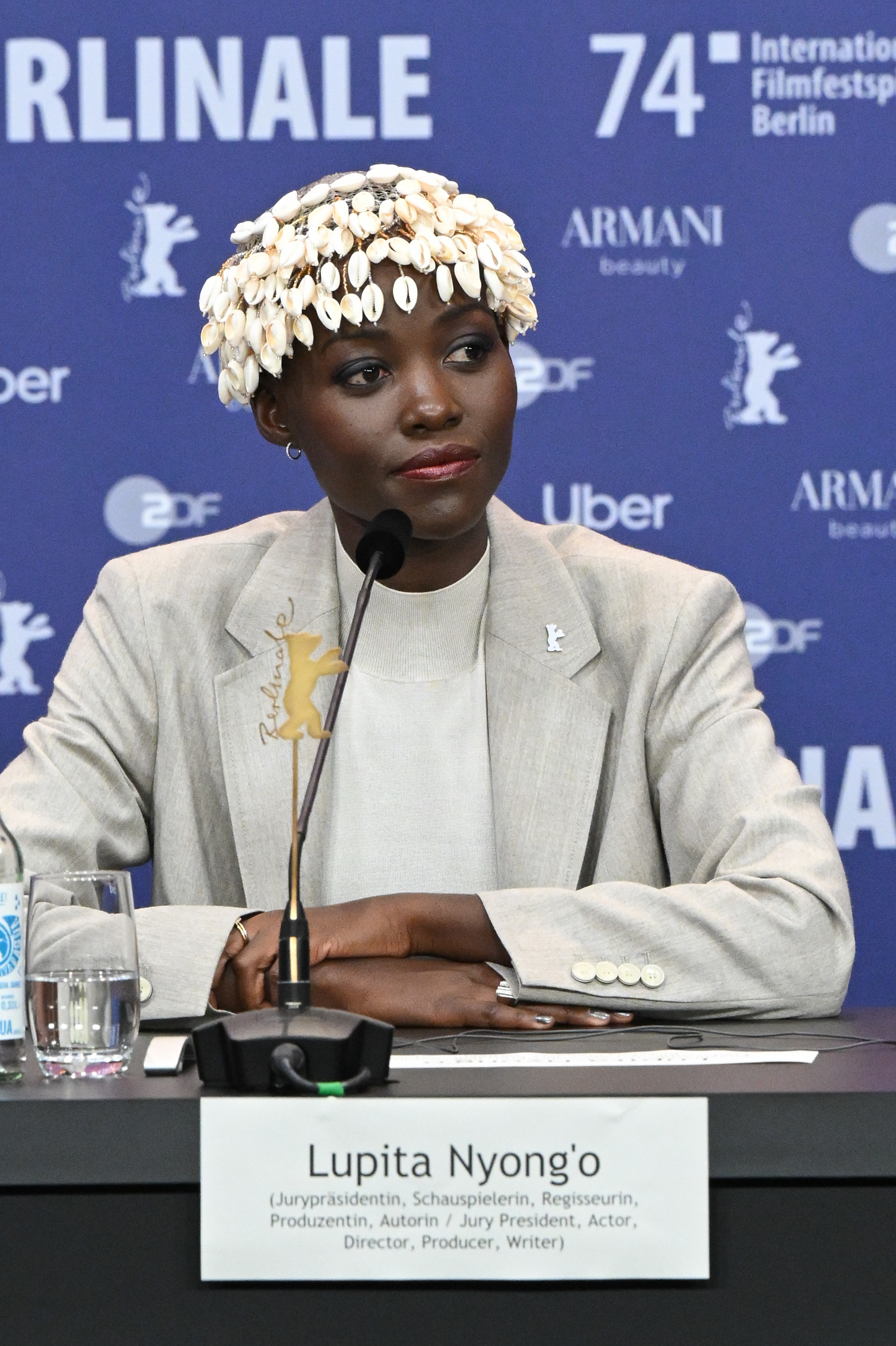 Lupita Nyong'o at a press conference for the 74th Berlinale International Film Festival, wearing a blazer and a headpiece adorned with white shells