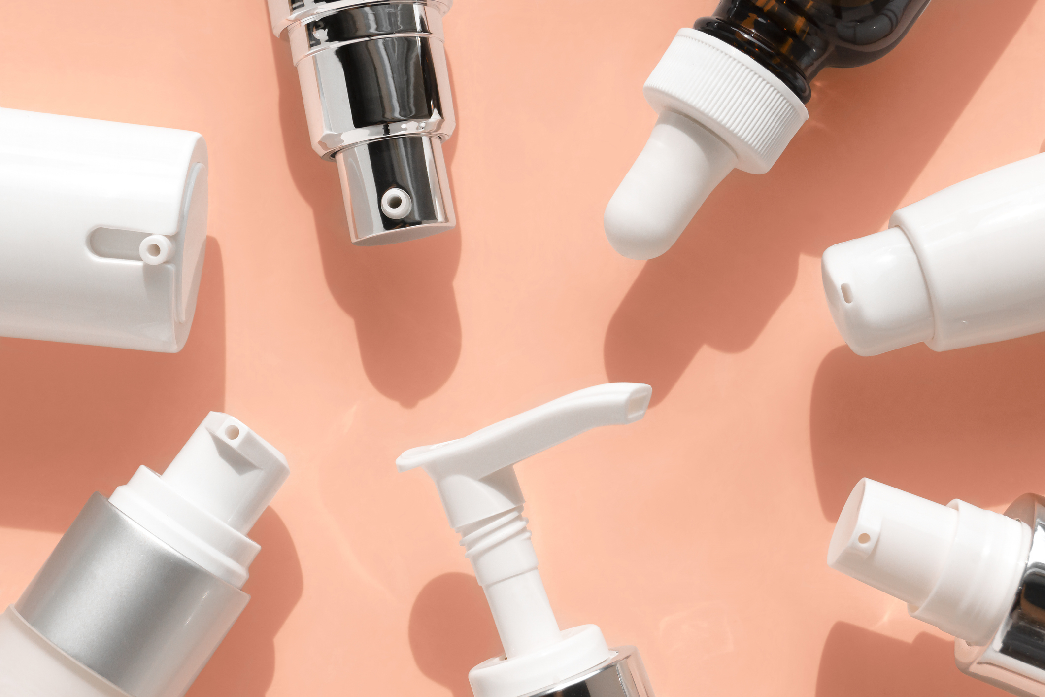 Various skincare product bottles with different types of dispensers, arranged in a circle on a light background