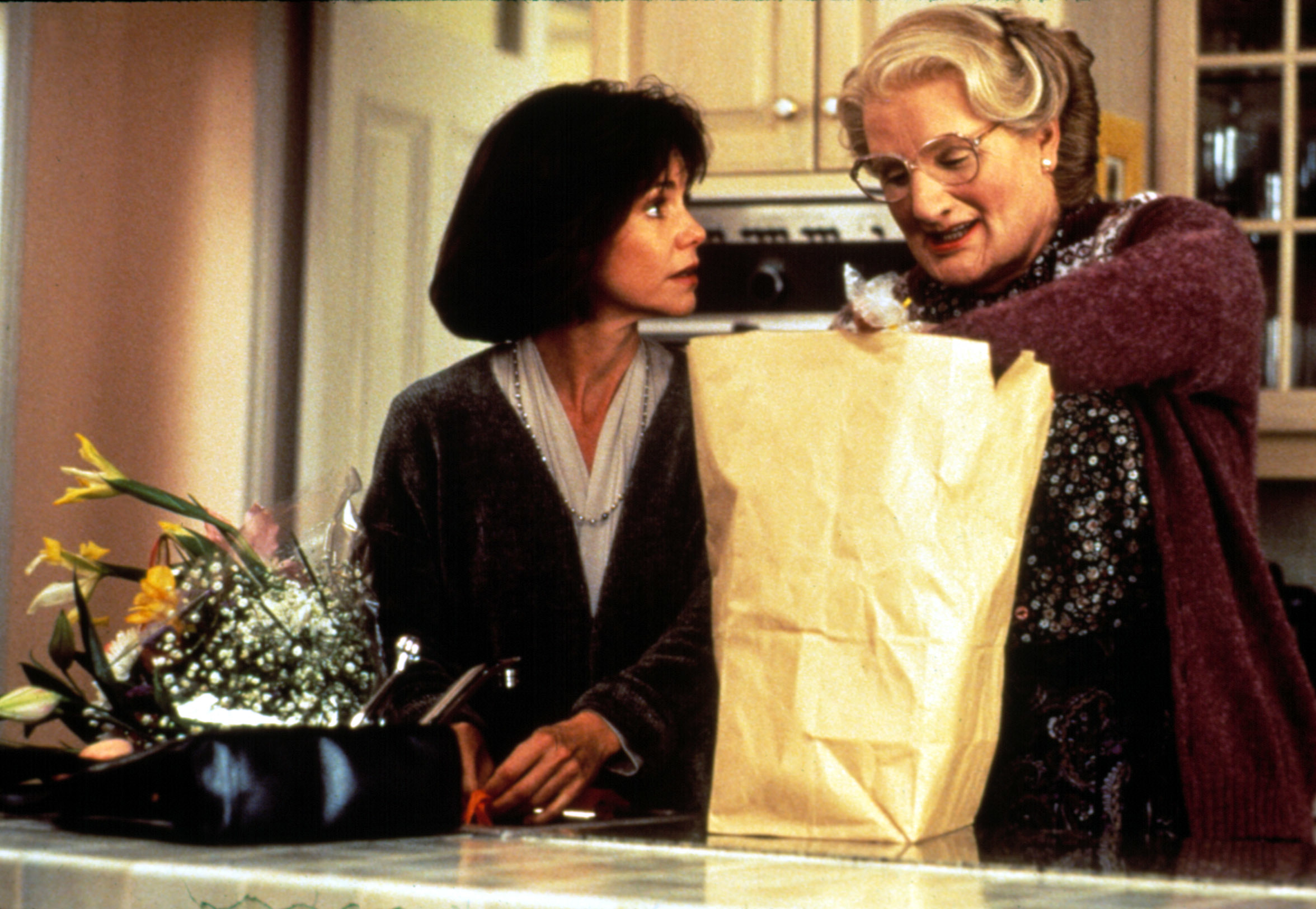 Two characters, played by Robin Williams and Sally Field, in a kitchen scene from the movie Mrs. Doubtfire. One holds a grocery bag