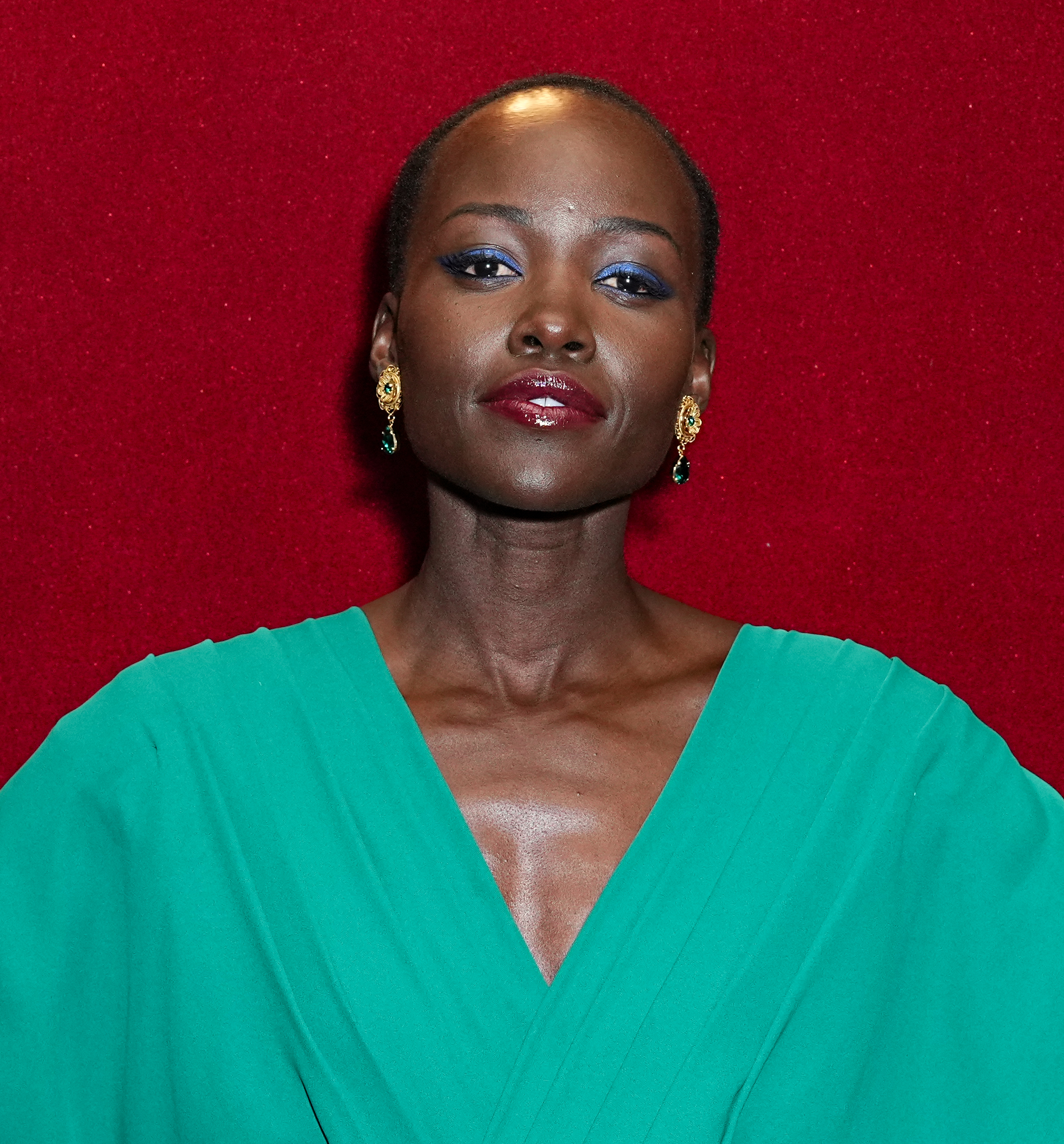 Lupita Nyong'o on the red carpet, wearing a V-neck green gown and gold earrings