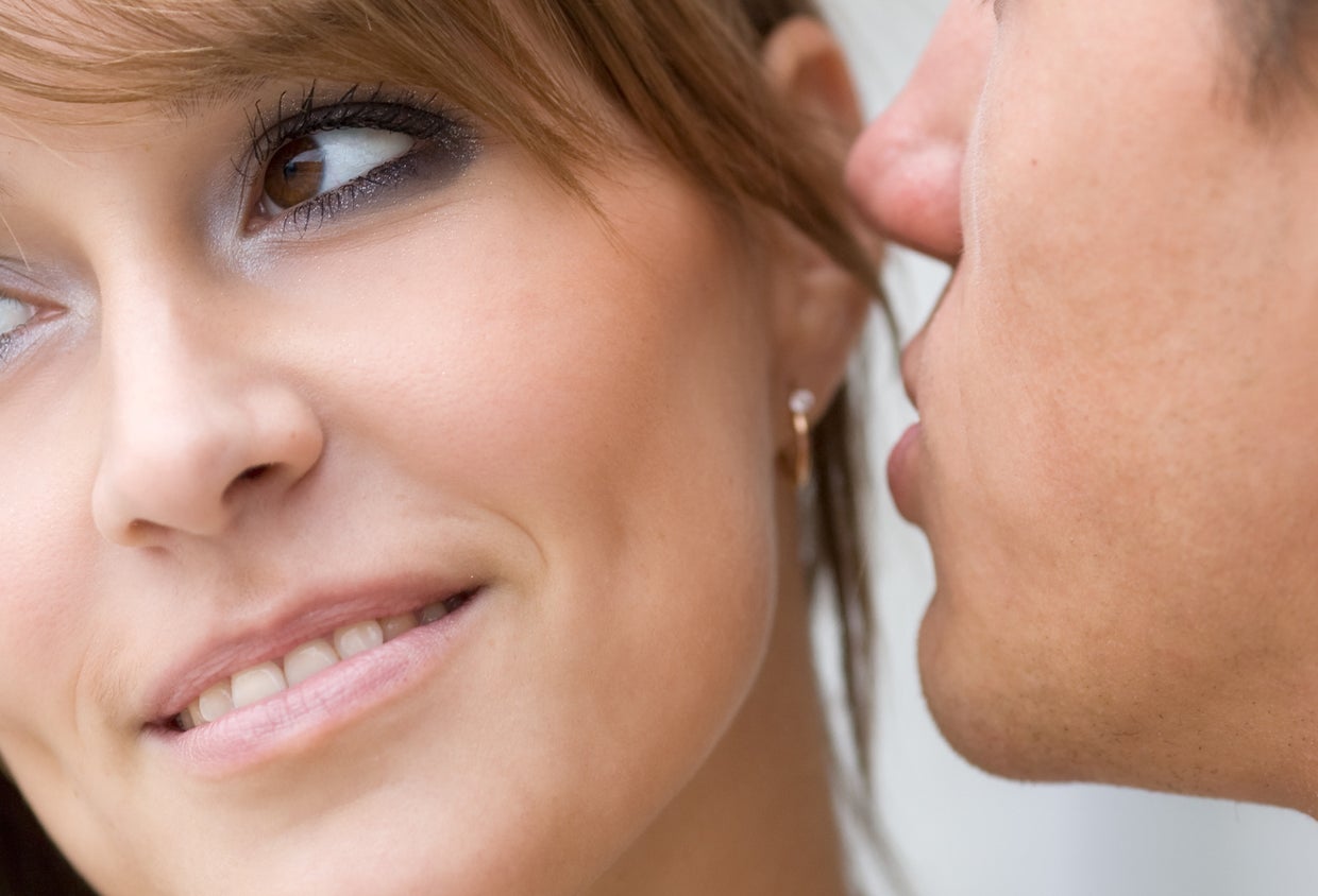 A woman smiles slightly while a man whispers into her ear. Names of the individuals in the image are unknown
