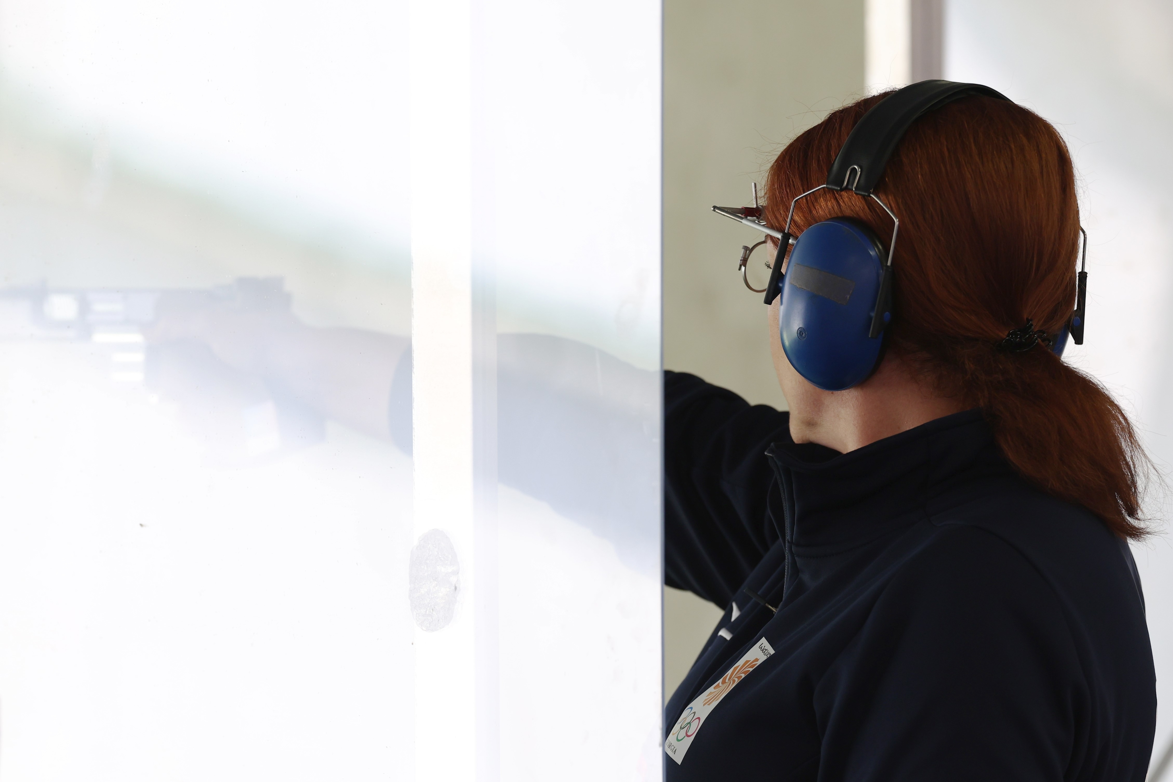 Una persona usa audífonos protectores y gafas mientras apunta una pistola en un entorno deportivo