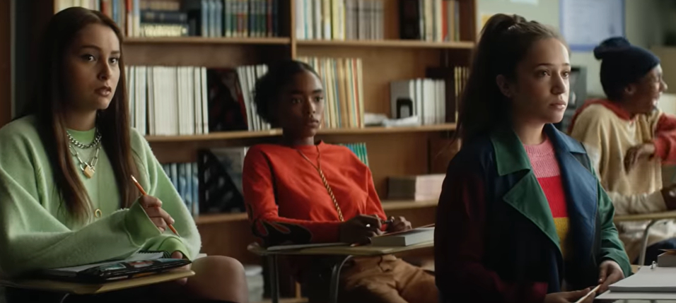 Several students sit attentively in a classroom filled with bookshelves