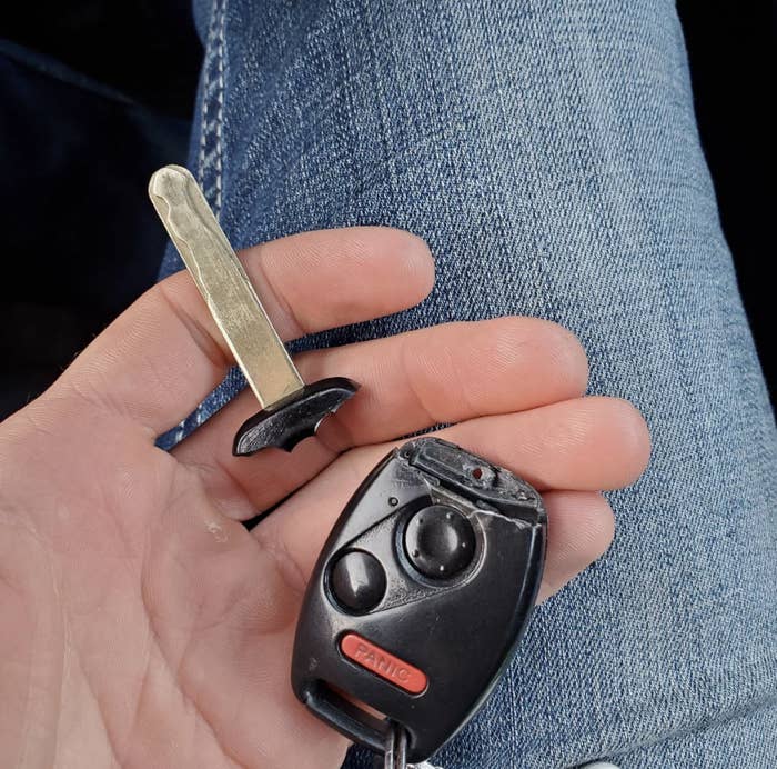 Person holding a detached car key blade and a car key remote in their hand over blue denim jeans