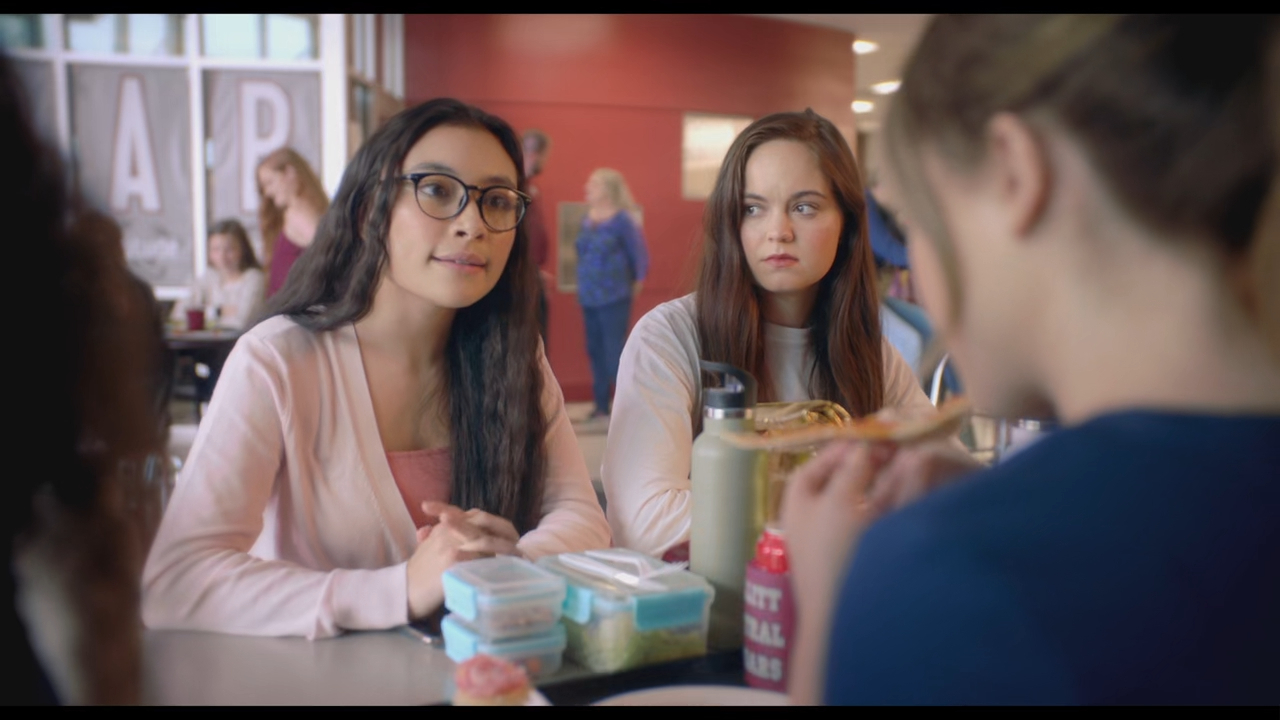 A group of girls are sitting at a table in a cafeteria, engaging in conversation.