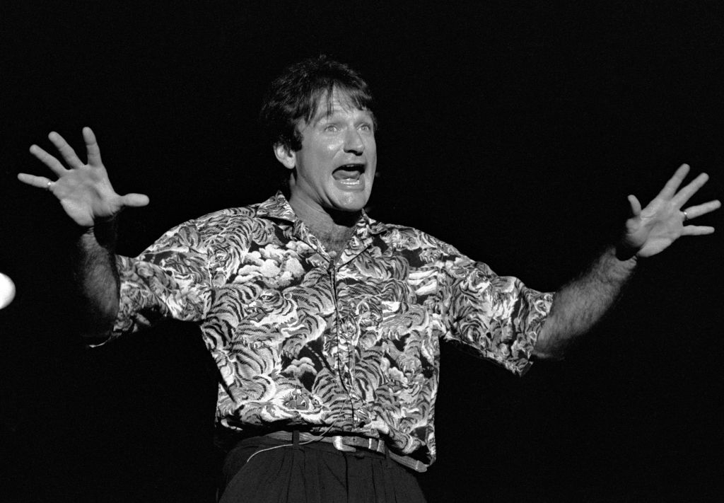 Robin Williams performing energetically on stage, wearing a patterned shirt and black pants