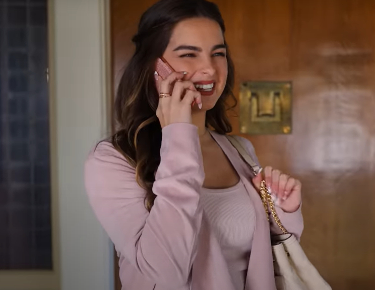 Addison Rae is smiling while talking on her phone and carrying a bag over her shoulder