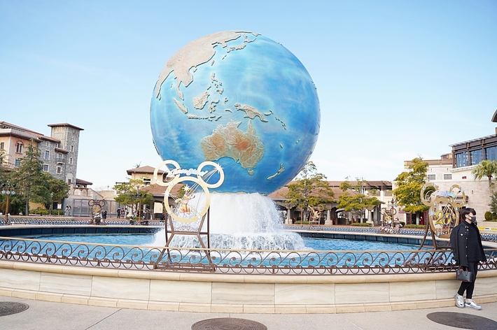 地球儀の噴水とミッキーマウスの装飾が施されたテーマパークの景色。背景には建物が見える。