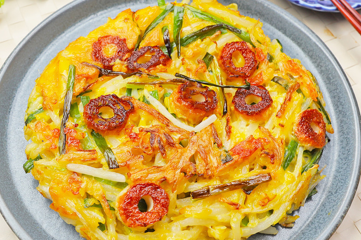 お好み焼きが盛り付けられたプレート、傍に醤油が入った小皿と箸が置かれている。