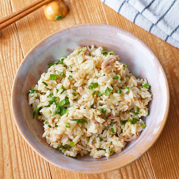 木製のテーブルの上に置かれた皿に盛られた炒飯。ネギと刻んだ肉が混ざっている。隣に箸と布巾が見える。