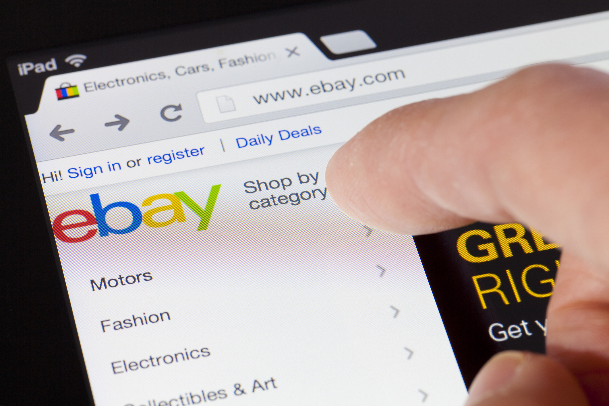 Close-up of a finger about to tap a category on the eBay website. The webpage displays categories like Motors, Fashion, Electronics, Collectibles &amp;amp; Art