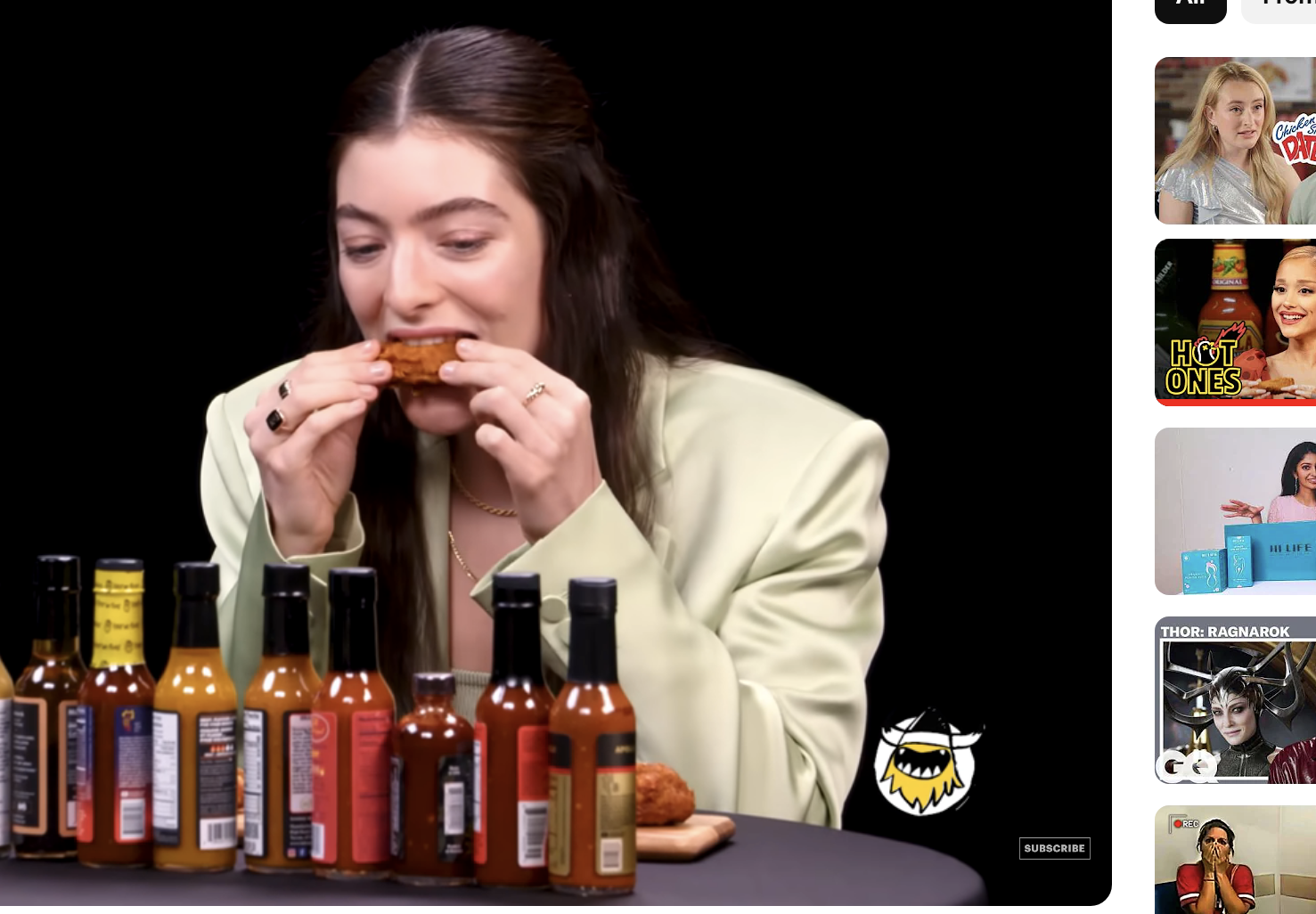 Lorde eating spicy wings on &quot;Hot Ones&quot; show, with various hot sauces on the table. Screenshot from YouTube titled &quot;Lorde Drops the Mic While Eating Spicy Wings | Hot Ones&quot;