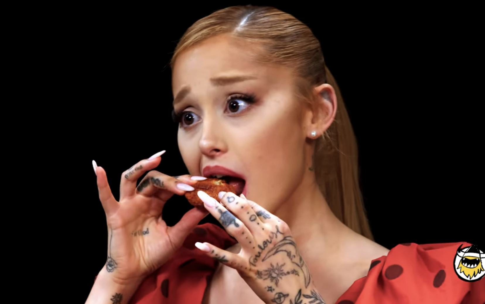 Ariana Grande eating spicy wings and reacting with wide eyes on the Hot Ones show. Various related video thumbnails are visible on the right side