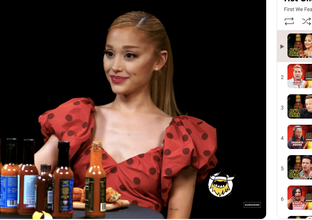 Ariana Grande is seen seated at a table with various hot sauces, participating in an interview on the show &quot;Hot Ones.&quot;