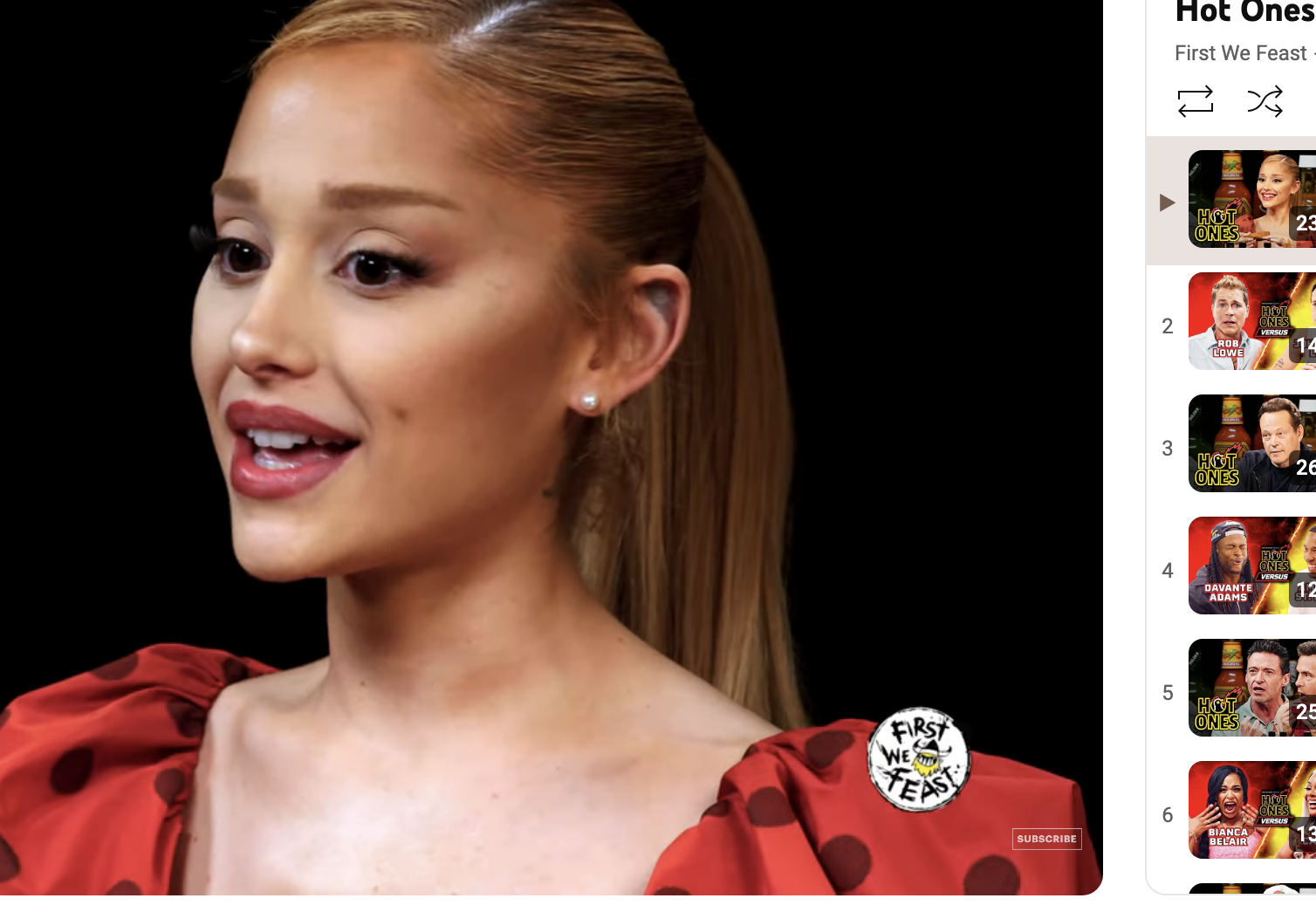 Ariana Grande on Hot Ones, talking while eating spicy wings. She is wearing a dress with puffed sleeves. The YouTube video page shows related videos on the right