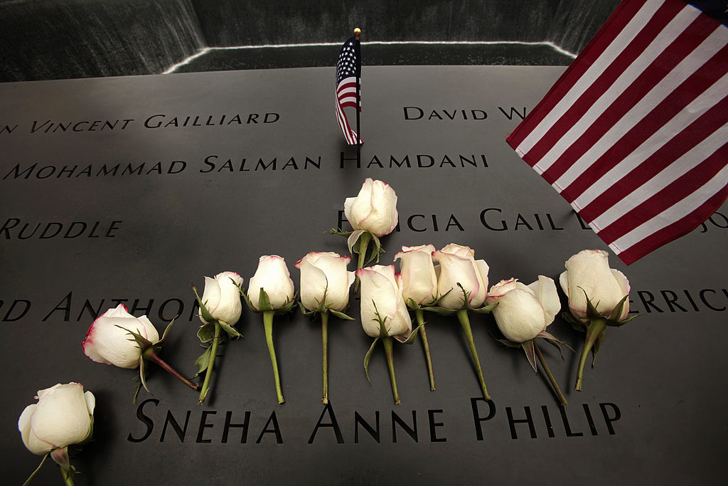 White roses and two American flags placed on the 9/11 Memorial, specifically near the name Sneha Anne Philip
