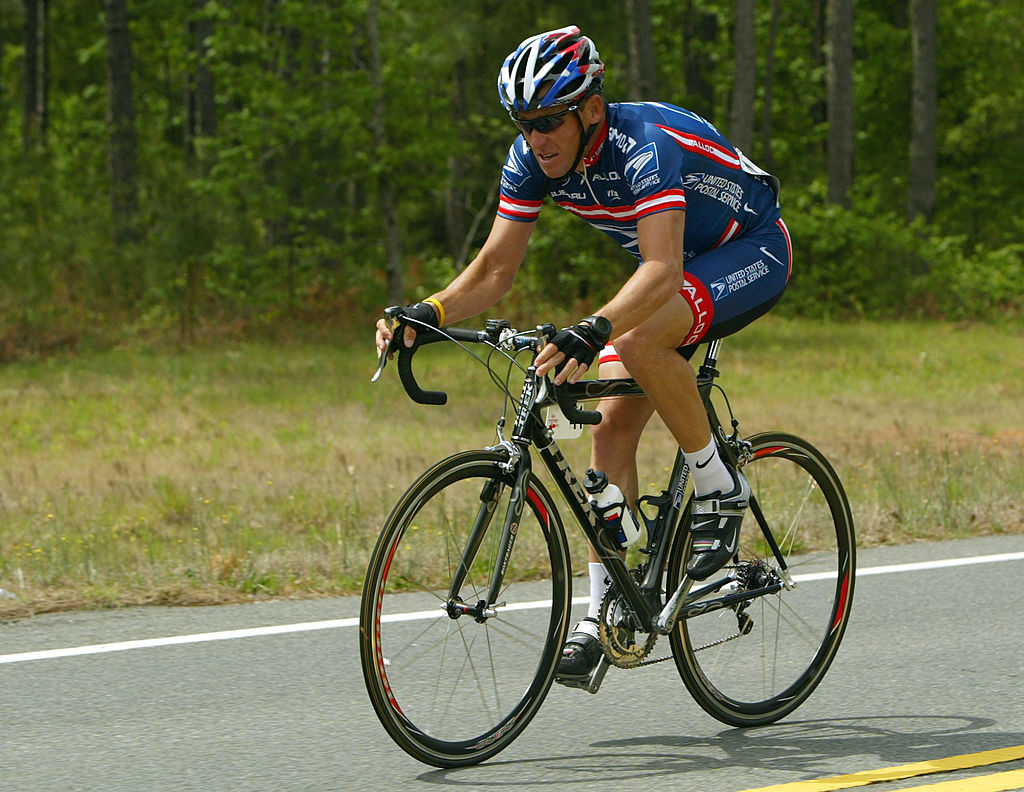 I don't know who these people are. A cyclist wearing a professional racing kit and helmet rides a road bike on a paved road, surrounded by greenery