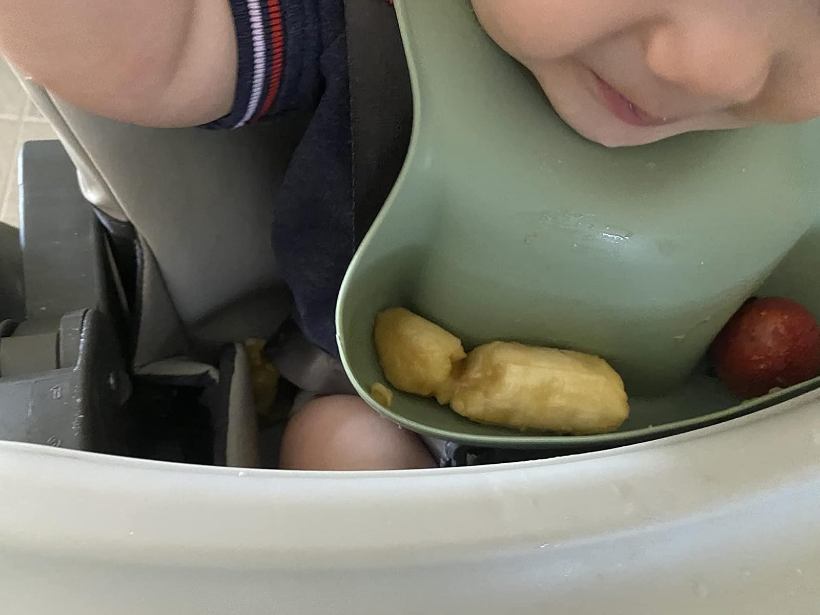 A babe  successful  a highchair with a silicone bib holding pieces of banana and a strawberry, appearing to smile