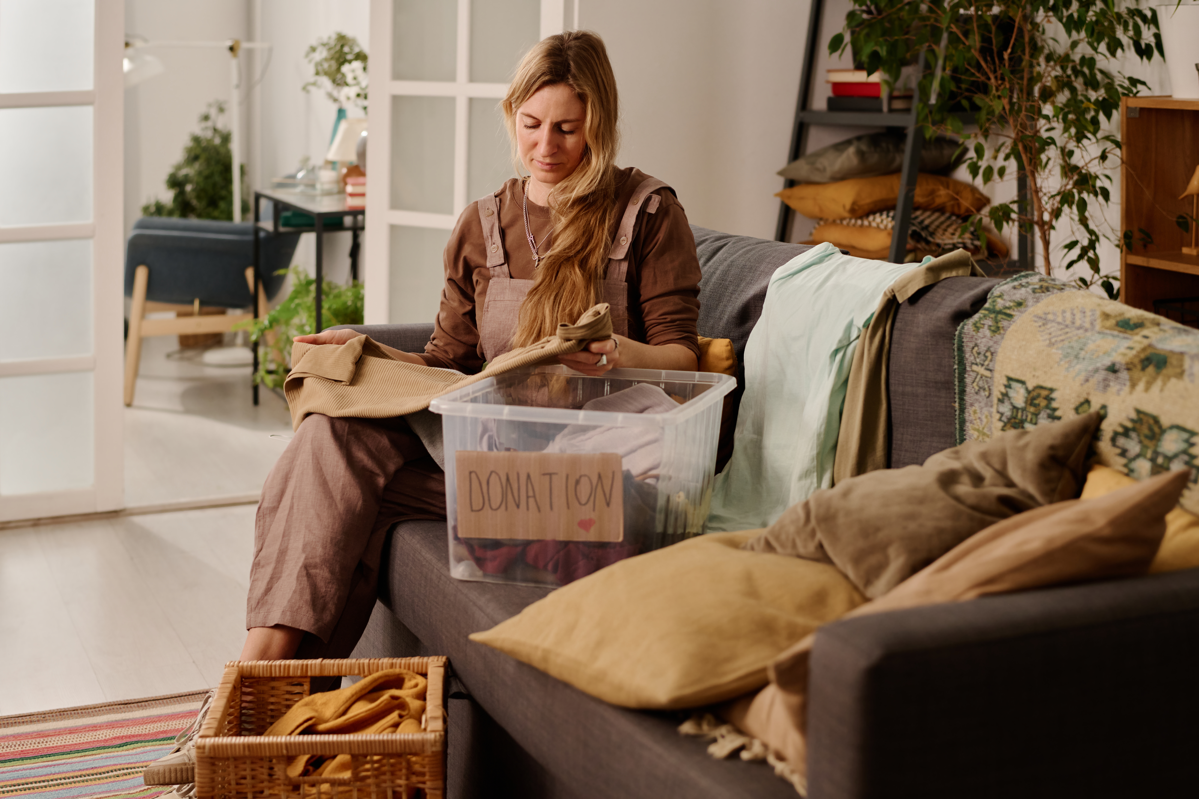 A woman sits on a couch sorting clothes into a donation box
