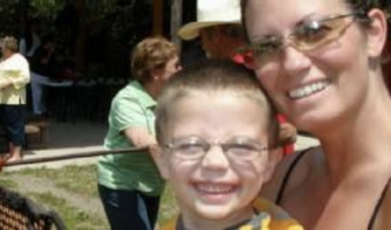A woman wearing sunglasses smiles with a young boy wearing glasses. People in casual attire are in the background. Names are unknown