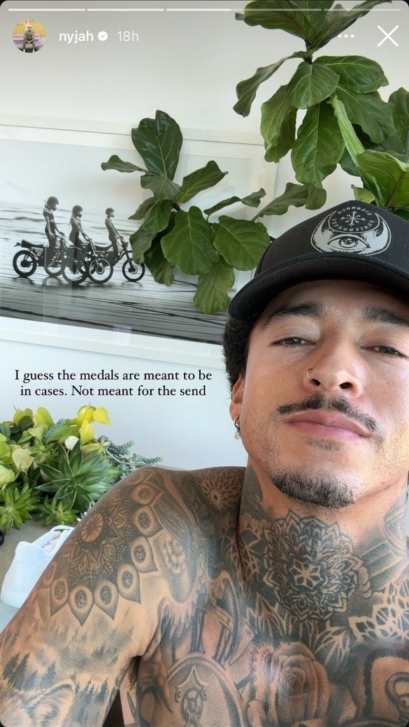 Nyjah Huston takes a selfie without his shirt on. Behind him, there is a black and white photo of motorcycles and a quote about medals in cases