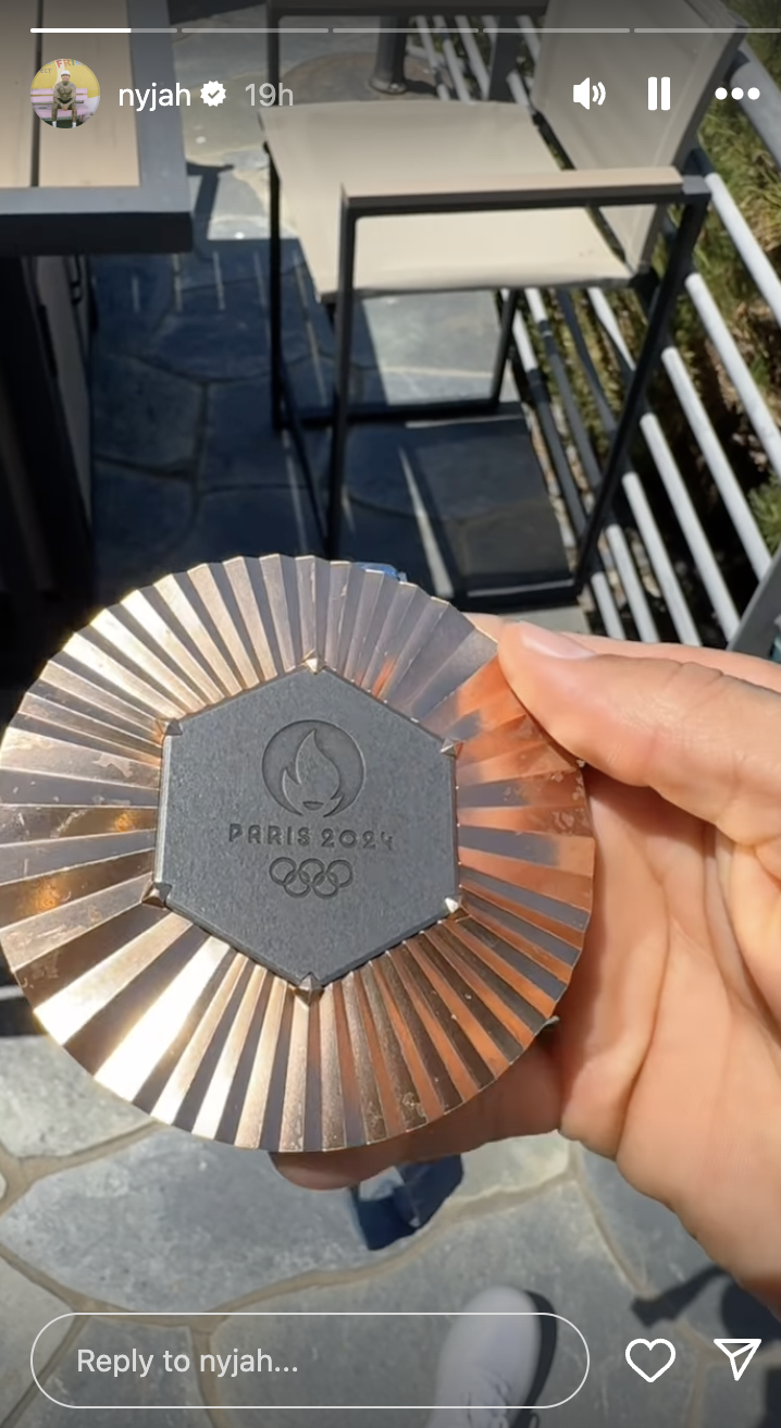Nyjah holds a round Paris 2024 Olympic Games medal with a hexagonal center and radial design