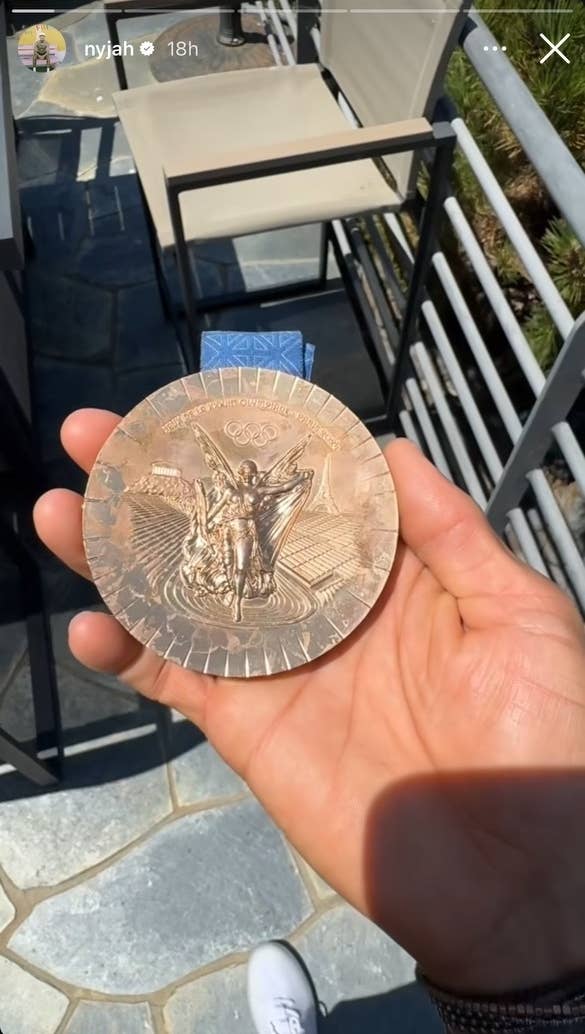 A person's hand holding a bronze Olympic medal featuring a figure of Nike, the Greek goddess of victory. Message options displayed at the bottom of the screen.