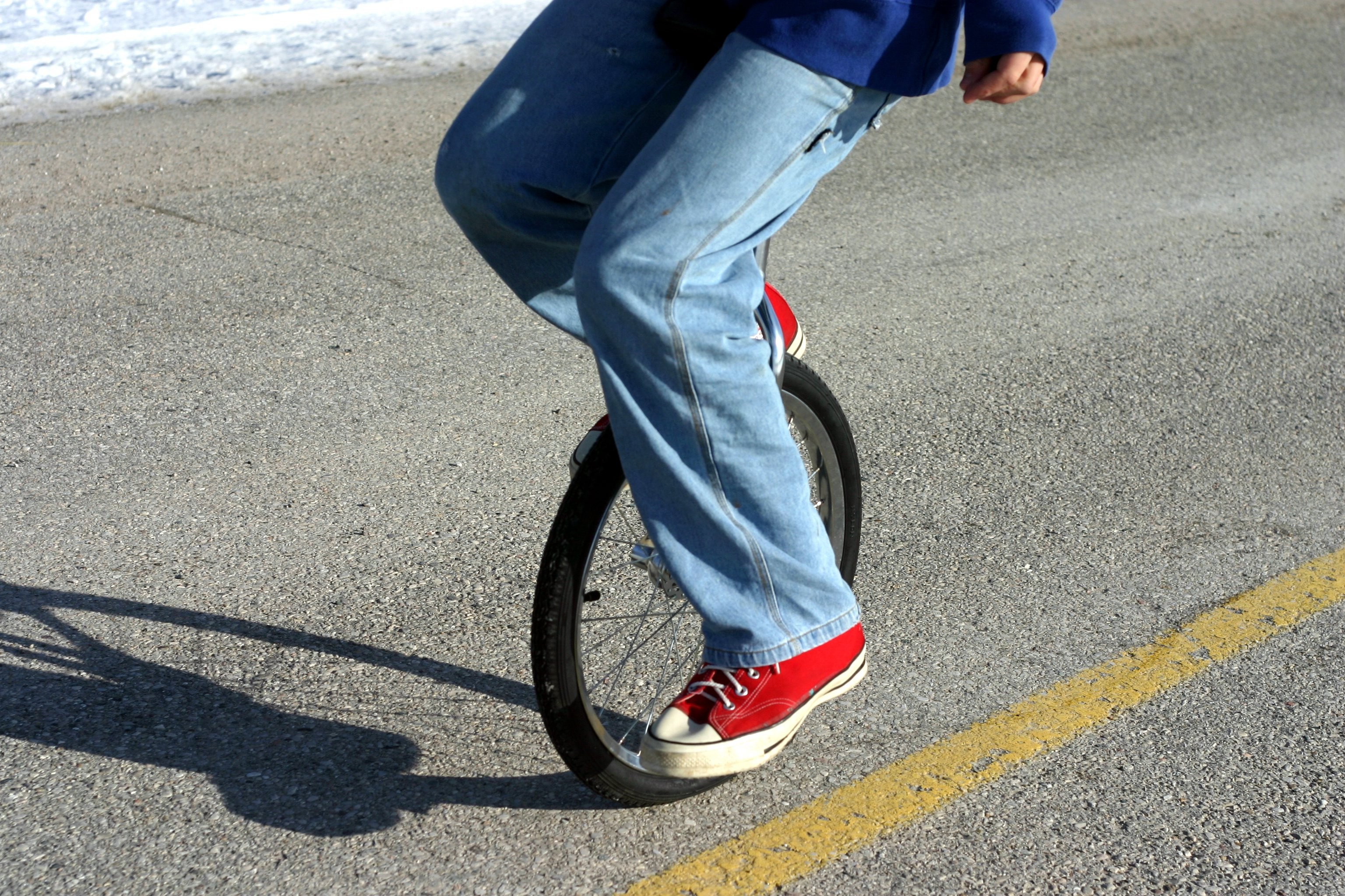 Person wearing jeans and red sneakers riding a unicycle on a road