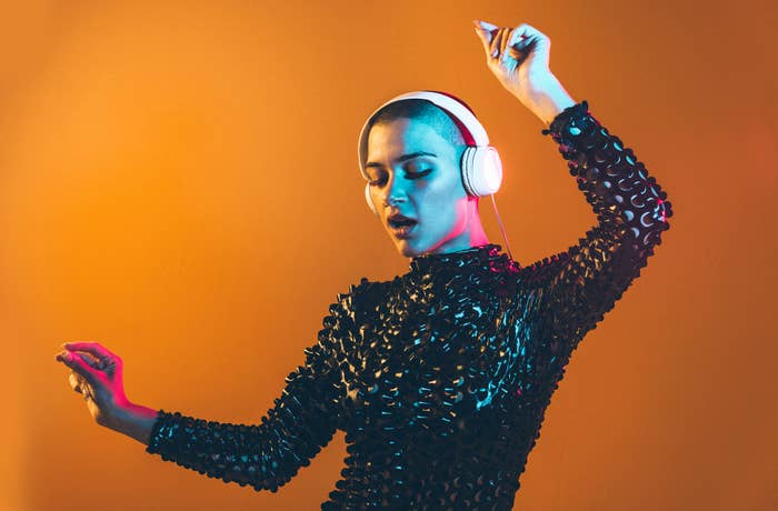 Person with headphones dancing, wearing a shiny, textured outfit. Hands raised, eyes closed, expressing a sense of immersion in the music