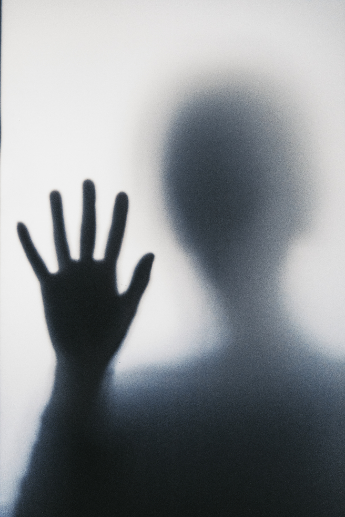 A blurred silhouette of a person's hand pressed against a frosted glass, creating a mysterious and abstract image