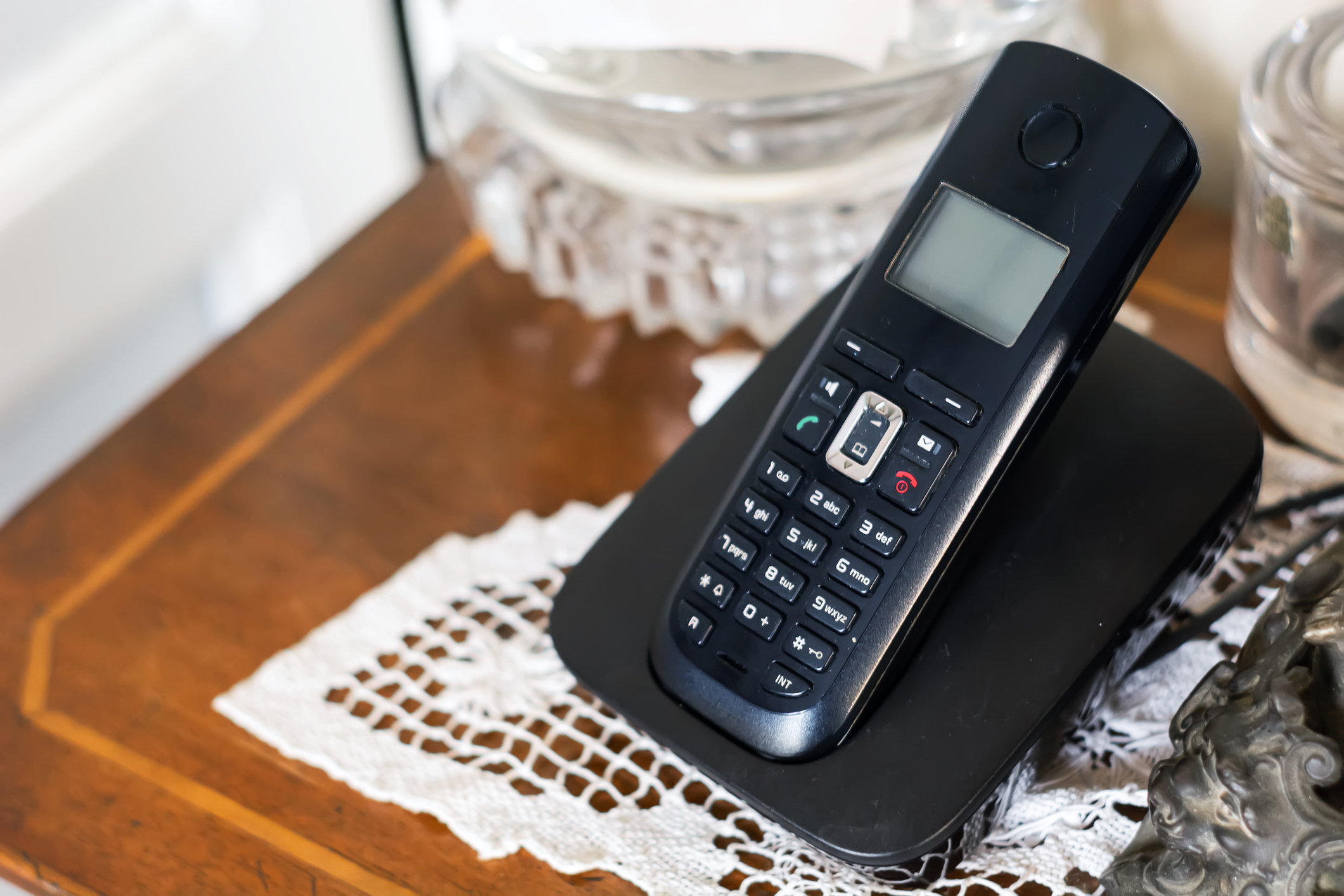 Cordless phone resting on a wooden table with a lace doily underneath
