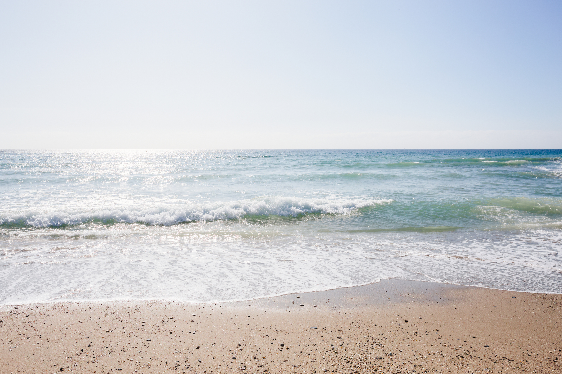 A serene beach with gentle waves washing onto the shore under a clear sky. No people are present